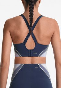 Marine sportbeha met kruis-achter ontwerp, met lichtgrijze en witte geometrische accenten. De stof lijkt glad met minimale stikdetails.