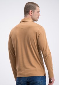 Koszulka polo z długim rękawem w kolorze beżowym z kołnierzykiem. Posiada boczny rozcięcie u dołu, gładką teksturę i nowoczesny krój.