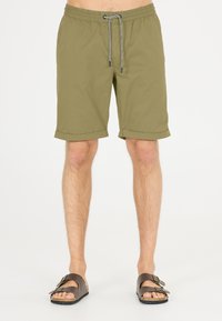 Olijfgroene shorts met een elastische tailleband en trekkoord; heeft omgeslagen mouwen. Gepaard met bruine sandalen met twee verstelbare banden.