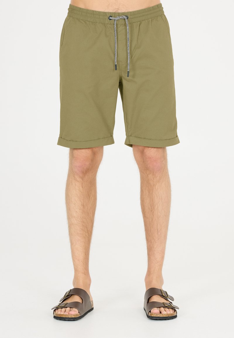 Olijfgroene shorts met een elastische tailleband en trekkoord; heeft omgeslagen mouwen. Gepaard met bruine sandalen met twee verstelbare banden.