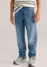 Svetlo modri kavbojki z ravnim krojem, petimi žepi in rahlim bledežem. Kombinirani z sivimi športnimi čevlji z mrežastimi poudarki.