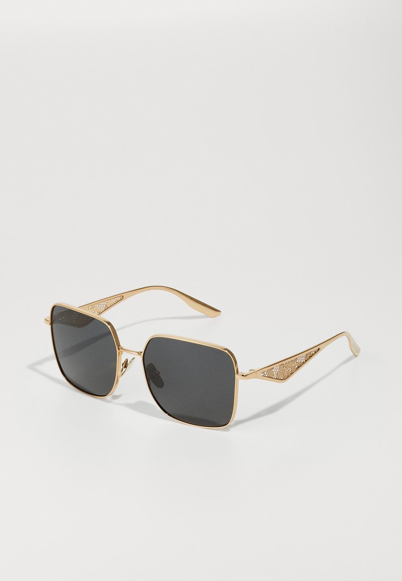 Gafas de sol de color dorado con forma cuadrada, lentes oscuros y elegantes adornos con patrones en las patillas. Montura de metal suave.