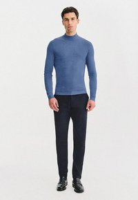 Niebieski, dopasowany sweter z golfem wykonany z miękkiego materiału, połączony z ciemnymi spodniami i czarnymi butami. Projekt jest elegancki z długimi rękawami.