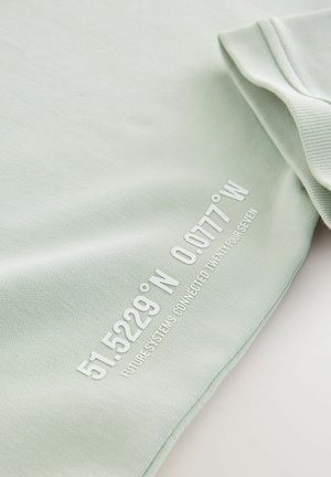 Helle grüne Baumwoll-T-Shirt mit rundem Ausschnitt. Mit weißem Drucktext: "51.5229° N 0.0777° W ZUKÜNFTIGE SYSTEME VERBUNDEN ZWANZIG VIER SIEBEN."
