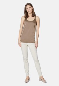 Bruine satijnen tanktop met een ronde hals, gecombineerd met witte slim-fit broek en lichtgrijze flats. Eenvoudige, gladde textuur en aansluitend ontwerp.
