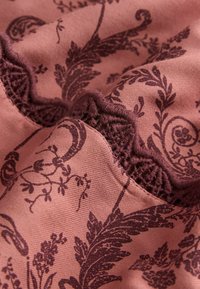 Soft pink fabric with dark purple intricate floral and leaf patterns and textured trim, shown in close-up folds.