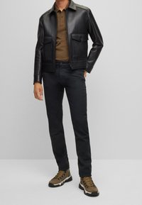 Mustaharma nahkarä jacket ku niln jäk dhokki, siena polo shirt, musta khusuka, ja siena badili kabḇa khuts ku niln bi cüṣlè.