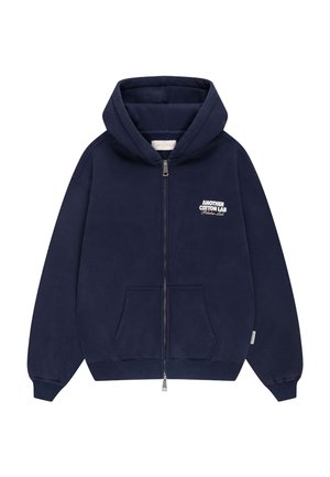 Sweat à capuche bleu marine zippé avec poches avant et texte blanc "Another Cotton Lab Pilates Lab" sur le côté gauche de la poitrine.