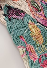 Flerfarvet mønstret stof med grønblå, pink og gule nuancer og en krøllet tekstur. Blomsterformer og detaljerede syninger er synlige.