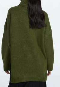 Pull tricot surdimensionné vert olive avec un col haut, des poignets et un ourlet côtelés, offrant une texture douce et une coupe décontractée.