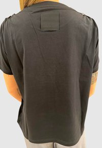 Sort T-shirt med korte ærmer lavet af blødt stof, med et firkantet mærke på den øvre ryg og dekorative knapper på skuldrene.