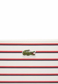 Portefeuille rayé en blanc, rouge et bleu marine, avec une finition texturée et un logo de crocodile brodé vert sur le devant.