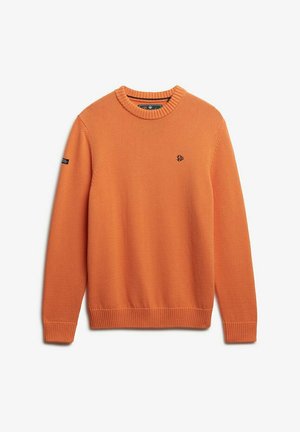 Pomarańczowy sweter crewneck z prążkowanym kołnierzykiem, mankietami i dole, z małym czarnym haftowanym logo na klatce piersiowej oraz czarną naszywką na lewym rękawie.