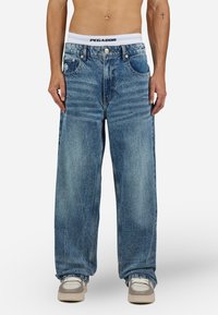 Light blue oversized denim jeans feature a straight-leg design with fading, five pockets, and a contrasting white logo waistband.