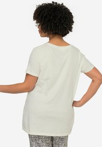 T-shirt in cotone beige chiaro con maniche corte, scollo rotondo e vestibilità rilassata, abbinato a pantaloni a righe zebrate black e white.