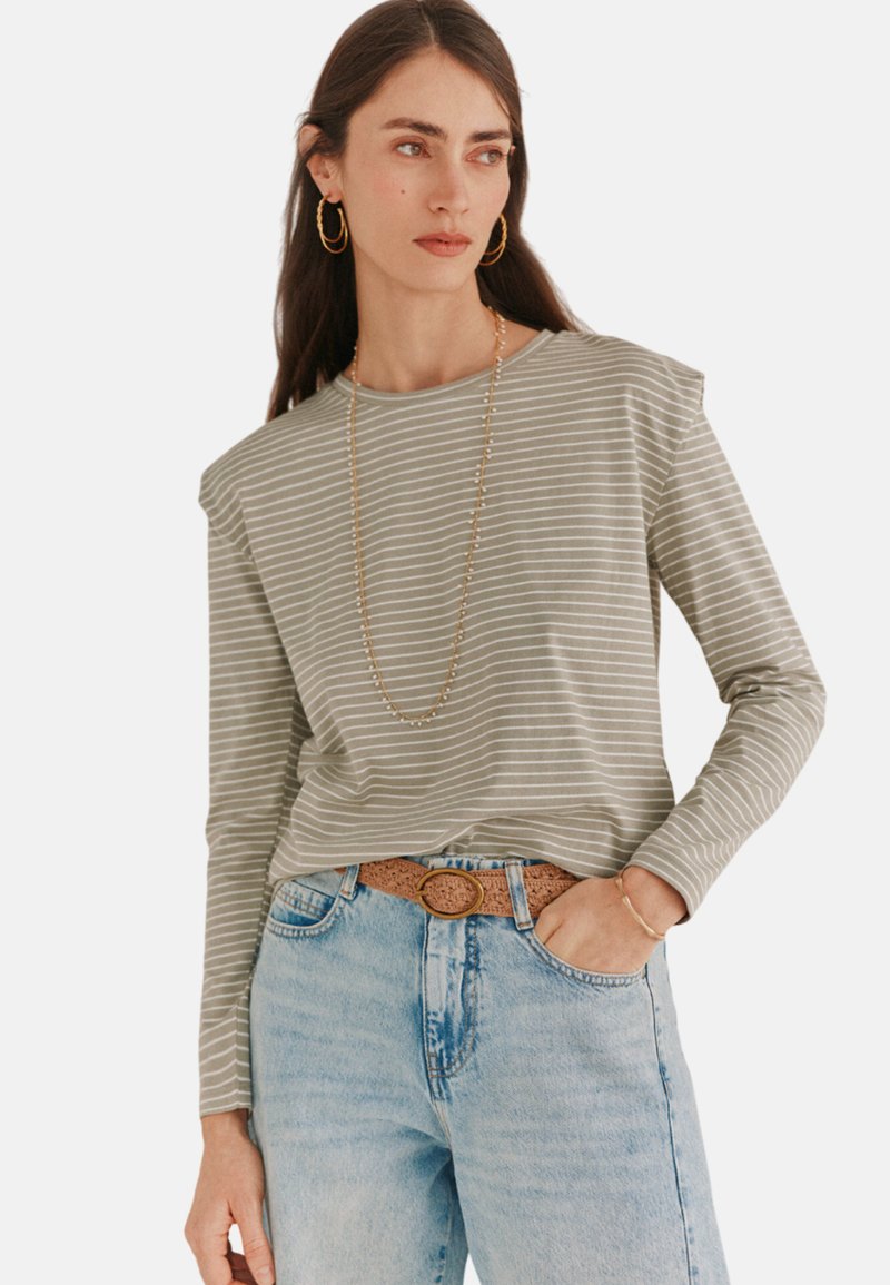 Langærmet stribet t-shirt i lys grøn og hvid med skulderdetaljer. Sammen med høj talje lys blå jeans og et tekstureret bælte.