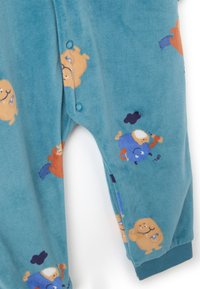 Un maillot de una pieza de forro polar azul con patrones de personajes de dibujos animados en naranja y púrpura. Cierres a presión en el cuello, puños acanalados en las mangas y los tobillos.