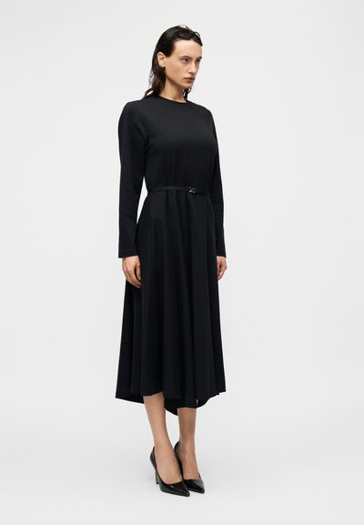 Μακρύ μαύρο φόρεμα από λείο ύφασμα, με στρογγυλή λαιμόκοψη, μακριά μανίκια και ψηλή μέση με μαύρη ζώνη. Κλασικός σχεδιασμός.