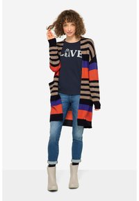 Färgglad lång cardigan med horisontella ränder i orange, blått, svart och beige, bärs över en marinblå t-shirt, ihop med jeans och beige stövlar.