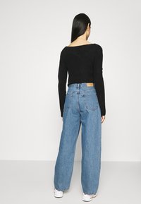 Musta ribbattu pitkähihaine villapaita, jota on käytetty korkeavyötäröisten vaaleansinisien leveälahkeisten farkkujen kanssa. Farkuissa on takana kielen muotoinen yksityiskohta ja löysä siluetti.