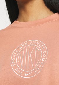 Pink Nike sweatshirt with a round logo featuring "NIKE" in the center and "SPORTS AND FITNESS COMPANY" around it; ribbed neckline.