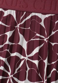 Tissu plissé bordeaux et blanc avec un grand motif floral et une ceinture bordeaux texturée partiellement visible avec texte en relief.