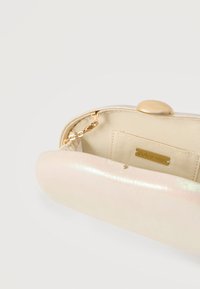 Μικρό τσαντάκι χειρός σε κρεμ απόχρωση με χρυσό κούμπωμα, ημίκλειστο που δείχνει μια χρυσή αλυσίδα και μια εσωτερική ετικέτα που γράφει "dolce vita."