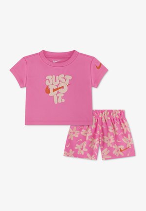 Rožinė kūdikių apranga su trumpomis rankovėmis marškinėliais, ant kurių užrašyta „JUST DO IT.“, ir šortais su šviesiai rožiniu gėlių raštu bei oranžinėmis Nike logotipų detalėmis.