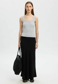Débardeur gris à côtes avec encolure larges associé à une longue jupe noire. Le mannequin tient un sac tote en crochet noir. Des chaussures plates noires viennent compléter le look.