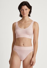 Svetloružový bralet a vysoko pásové nohavičky vyrobené z mäkkej tkaniny. Bralet má široké ramienka a hladký povrch.