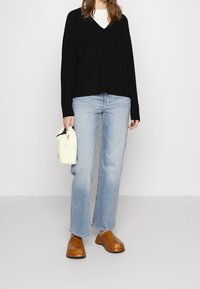 Schwarzer gerippter Strickpullover mit V-Ausschnitt, hellblaue gerade Jeans, braune Clogs und eine kleine cremefarbene Tasche mit einer Tasche.