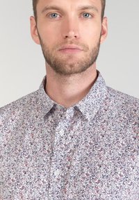 Camicia con bottoni dalla vestibilità classica, caratterizzata da uno sfondo bianco e un piccolo motivo floreale nei toni del rosa e del blu navy. Colletto classico e chiusura a bottoni standard.