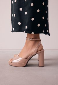 Testszínű lakkbőr magas sarkú szandálok vastag sarokkal és nyitott orral, bokapánttal és csattal, sima felülettel.