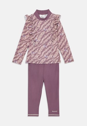 To-delt barneklær bestående av en langermet topp med volangdetalj og blomstermønster i lilla, sammen med ensfargede lilla leggings.