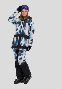 Strój narciarski w wielokolorowym wzorze niebieskim, różowym i białym. Zawiera zapinaną na zamek kurtkę z czarnymi akcentami oraz czarne spodnie narciarskie.