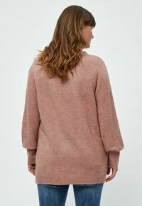 Übergroßer rosa Strickpullover mit strukturiertem Finish, mit überschnittenen Schultern und gerippten Bündchen. Getragen über blauen Jeans, zeigt die Rückenansicht.