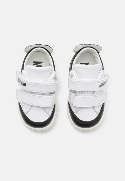 Zapatillas de niños con diseño de cuero blanco y negro, que cuentan con dos tiras de velcro y punta redondeada. Logo impreso en el lateral.
