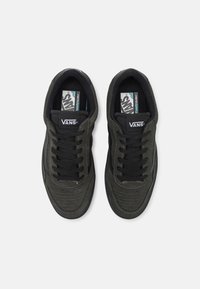 Black suede sneakers features perforated detailing, flat black laces, and a white logo. The design includes contrasting black accents.