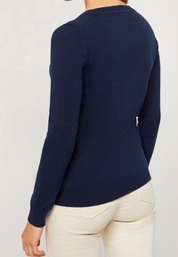 Navy modrý svetr s dlouhými rukávy, těsně přiléhavého střihu a ribovaným lemem. Měkká textura s klasickým kulatým výstřihem. Pohled zezadu ukazuje bezproblémové ramena.