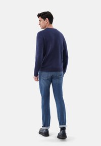 Maglione a maglia blu navy con maniche lunghe, polsini e orlo a coste, abbinato a jeans in denim azzurro chiaro e scarpe nere. La ragazza ha i jeans arrotolati sui polsini.