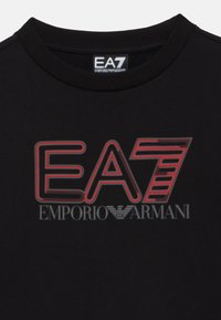 Čierne tričko s červenobielym logom „EA7“ so pruhovanými akcentmi a textom „EMPORIO ARMANI“ pod ním, okrúhly výstrih.