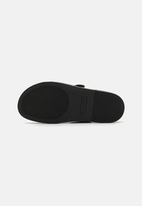 Black slip-on shoe sole featuring textured rubber for grip, with a rectangular logo, minimalist design, and smooth edges.
