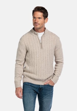 Pull en maille beige clair avec un col zippé à mi-hauteur, présentant une texture côtelée et des poignets ajustés, associé à un jean bleu.