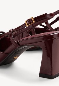 Bordeaux leren hooggehakte sandalen met glanzende finish, voorzien van kruisende banden, een gouden gespte, en een gestructureerde blokhak.