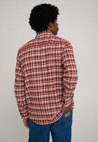 Camicia a quadri rossa e beige con maniche lunghe, colletto e orlo curvo, realizzata in tessuto leggero. Presenta una finitura testurizzata.