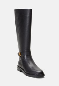 Juodos odinės iki kelių ilgio botai su tekstūruota paviršiumi, plokščiu kulnu ir šonine juosta su auksiniu emblem. Klasikinis dizainas, tinkantis įvairiems drabužiams.