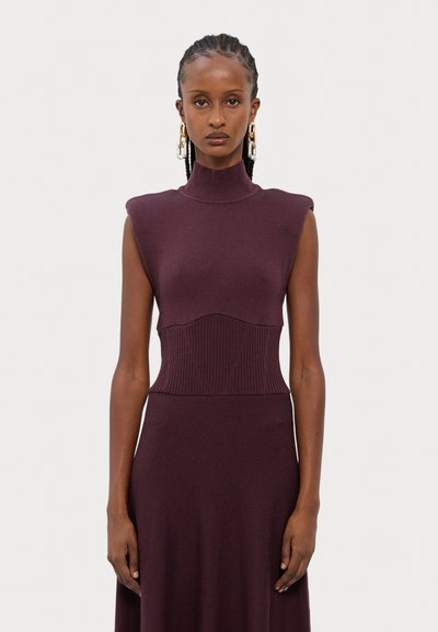 Sleeveless, turtleneck dress in deep burgundy, featuring ribbed texture at waist and shoulders, with a flowing bottom.