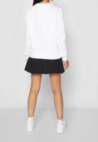 Felpa bianca a maniche lunghe, con polsini a costine, vestibilità comoda, abbinata a una gonna nera a pieghe e sneakers bianche. Design semplice e sportivo.
