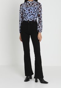 Jeans neri a palazzo abbinati a una blusa trasparente blu a maniche lunghe con stampa leopardata nei toni del marrone e del nero. Stivali neri lucidi con tacco.