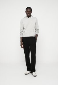 Gray hooded sweatshirt with a front pocket, paired with black tapered pants and white sneakers featuring gray and black accents.